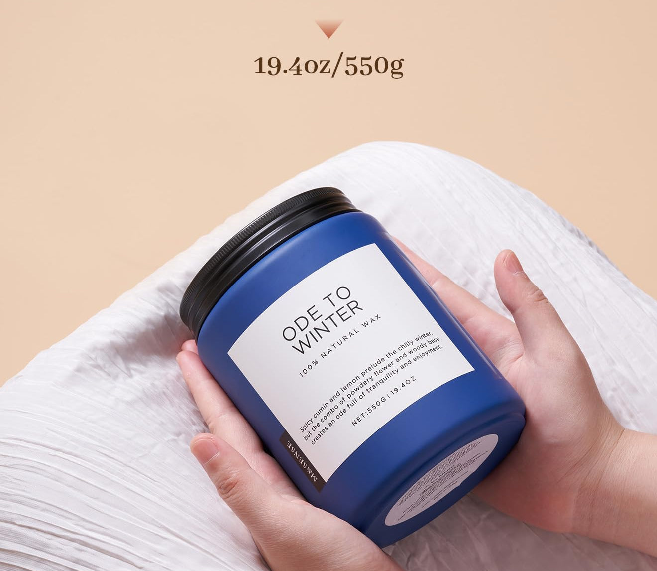 Blue candle labeled 'Ode to Winter' held by a hand with beige background