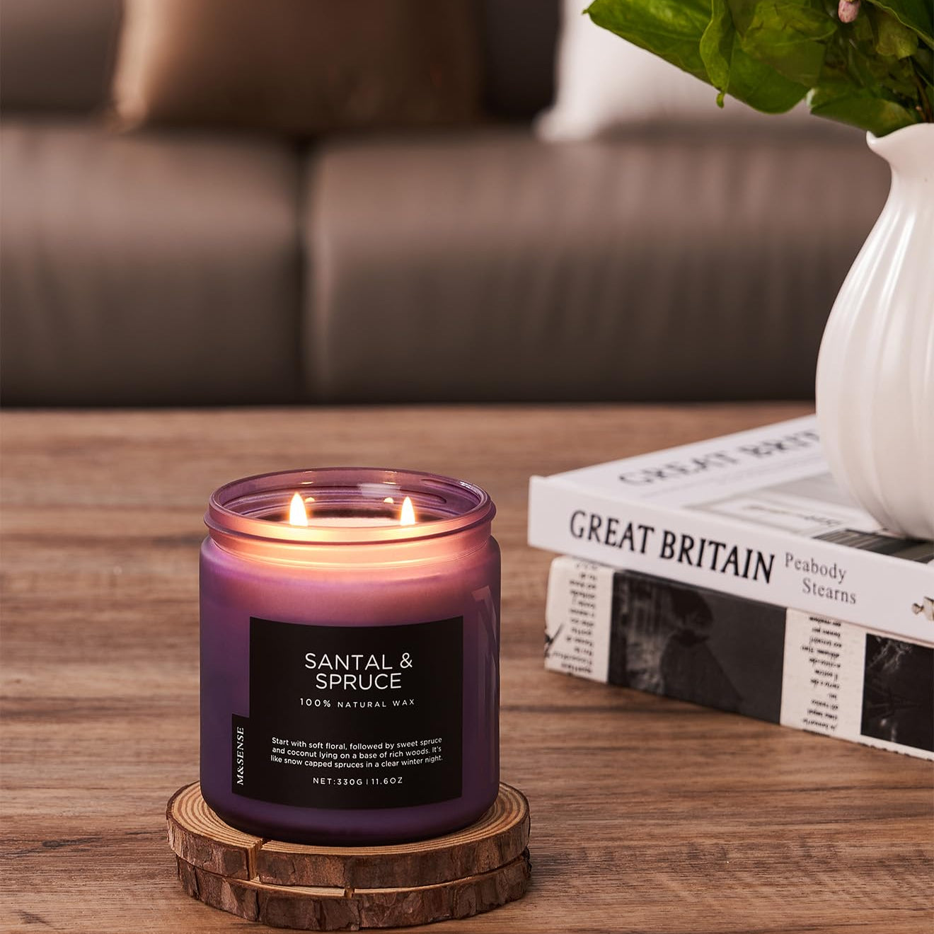 Scented candle with wooden coaster on a table with a blurred sofa and book in the background