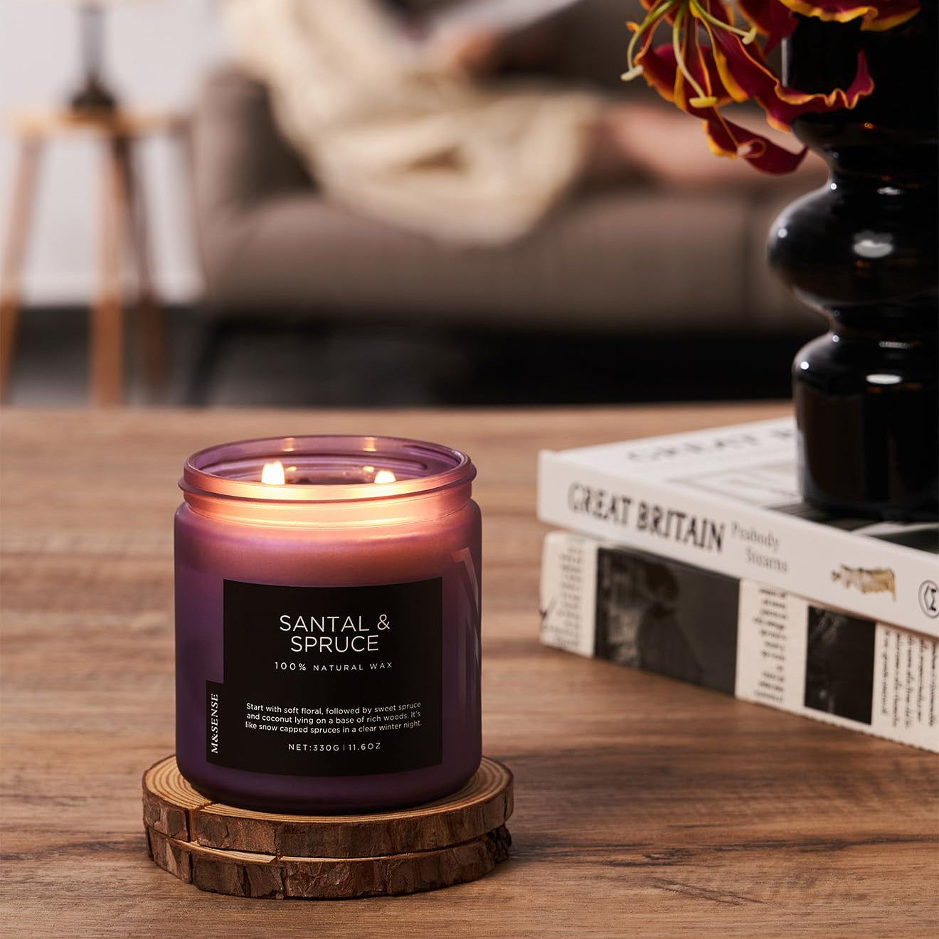 Santal & Spruce candle on a wooden coaster with a blurred background of a cozy living room.