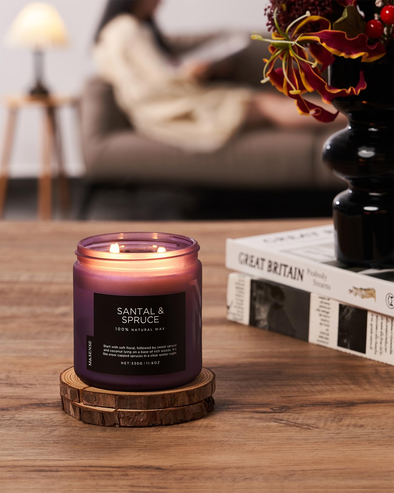 Santal & Spruce candle on a wooden coaster with a blurred background of a cozy living room.