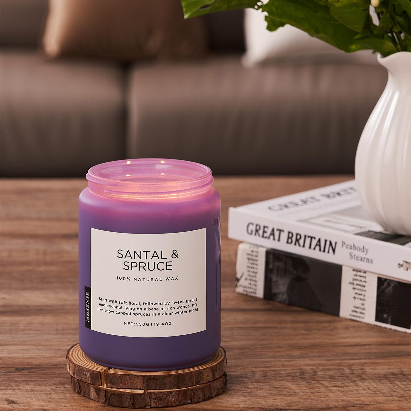 Purple candle labeled 'Santal & Spruce' on a wooden coaster with a vase and newspaper in the background.