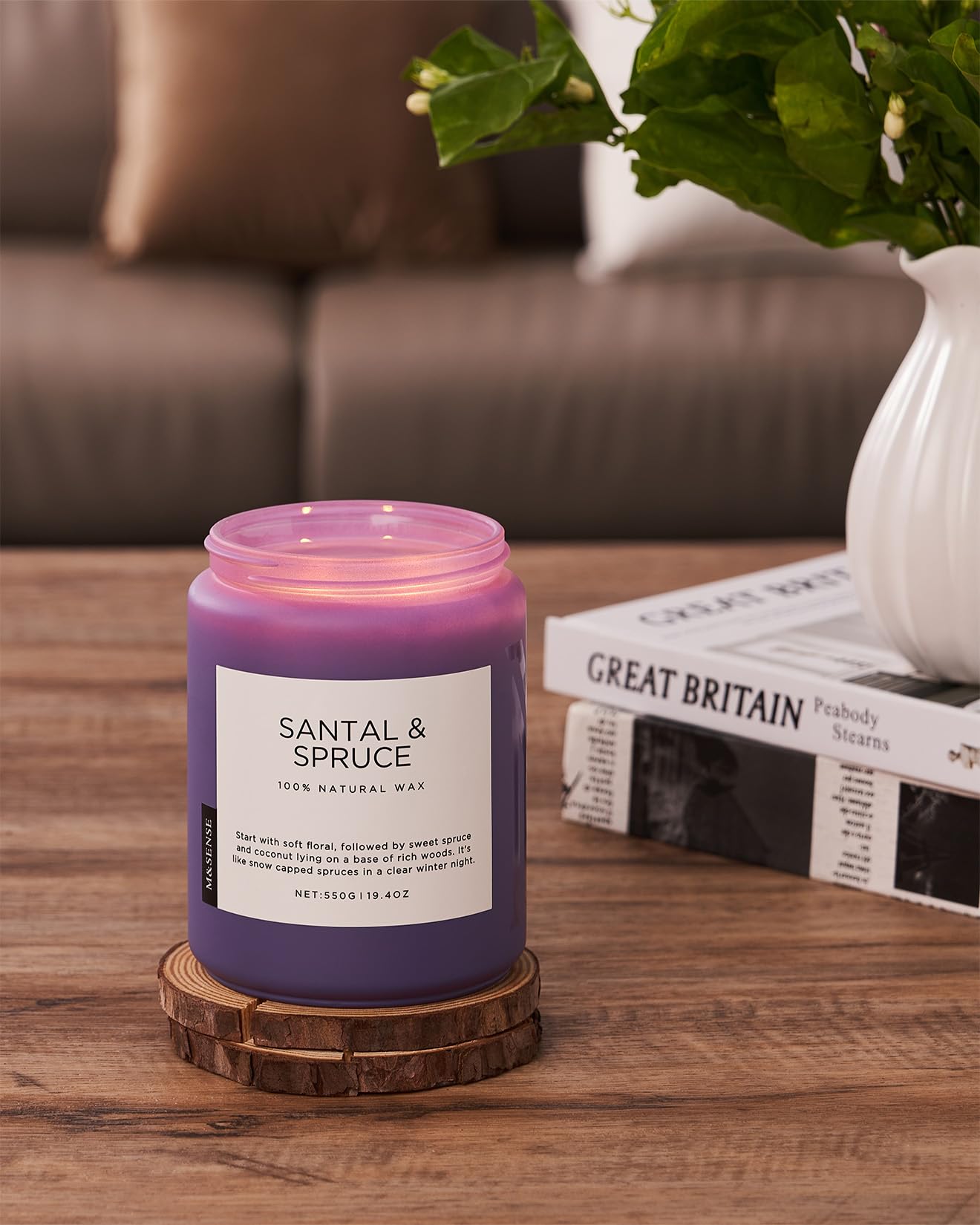 Purple candle labeled 'Santal & Spruce' on a wooden coaster with a vase and newspaper in the background.
