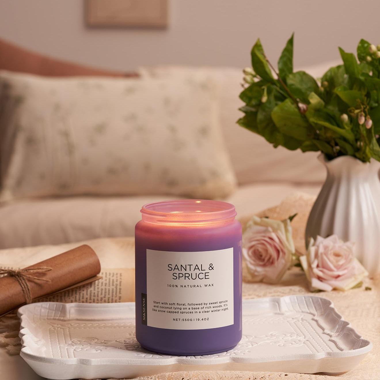 Santal & Spruce candle on a table with flowers and a blanket in the background