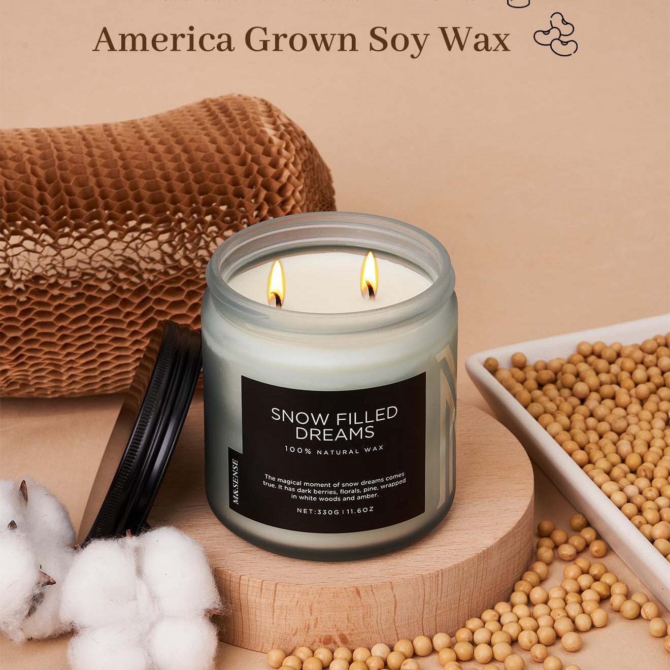 Candle with 'Snow Filled Dreams' label, surrounded by cotton, soybeans, and a woven basket on a beige background.