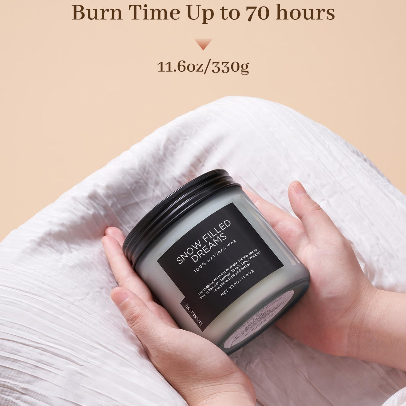 Candle labeled 'Snow Filled Dreams' held by a hand with beige background and text about burn time.