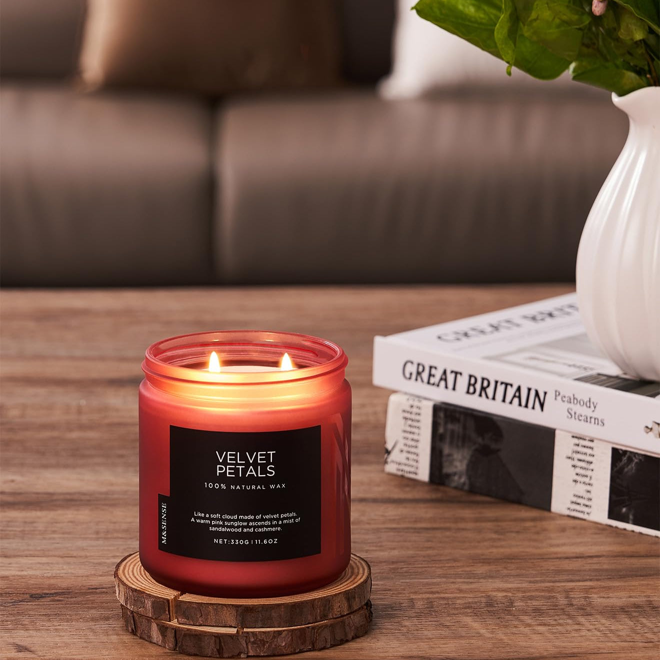 Red candle with a wooden coaster on a table, with a blurred background of a couch and books.