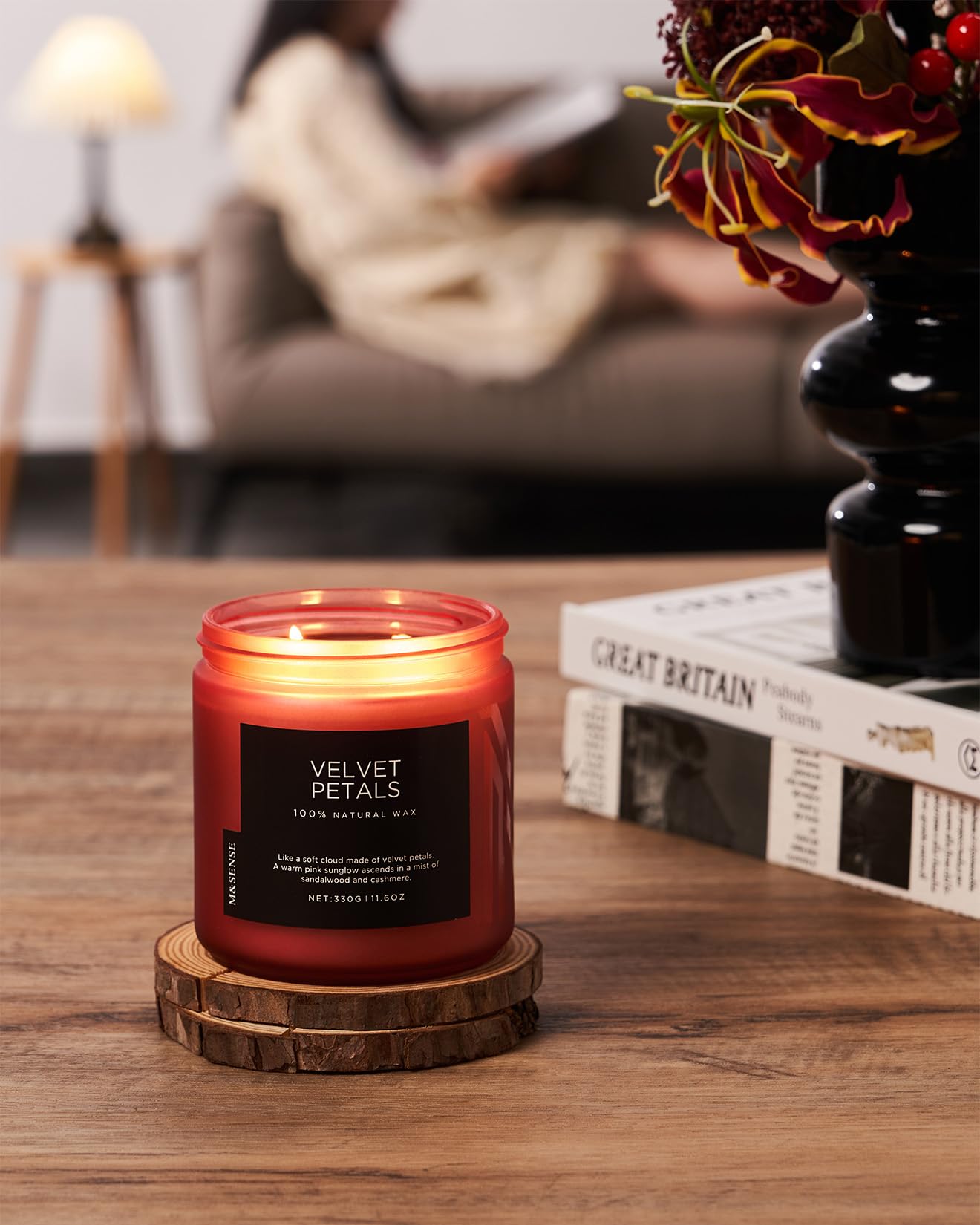 Candle labeled 'Velvet Petals' on a wooden coaster with a blurred background of a person reading.