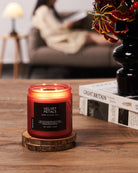 Candle labeled 'Velvet Petals' on a wooden coaster with a blurred background of a person reading.