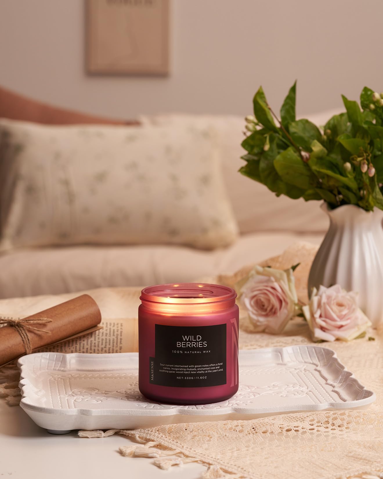 Candle labeled 'Wild Berries' on a table with a vase of flowers and a blanket in the background