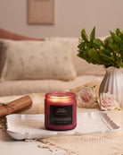Candle labeled 'Wild Berries' on a table with a vase of flowers and a blanket in the background