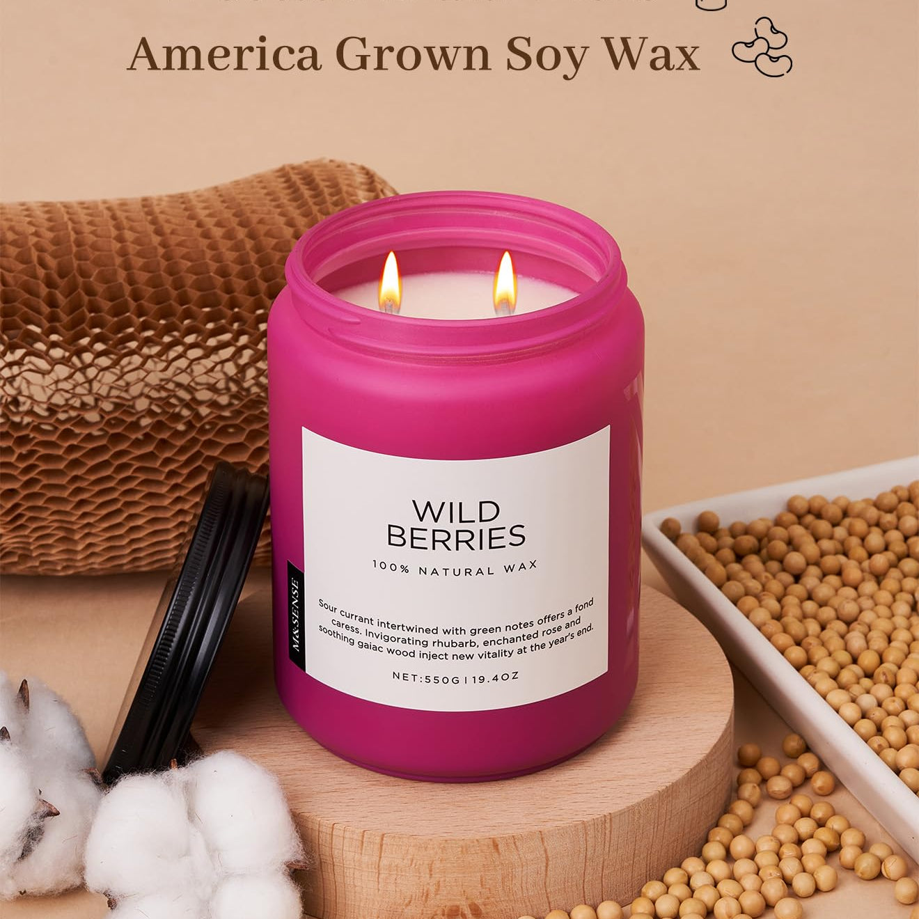 Pink candle with 'Wild Berries' label on a wooden surface with soybeans and cotton.