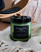 Eucalyptus mint scented candle in a green frosted jar, adding a fresh aroma to a cozy living room setting with a sofa.