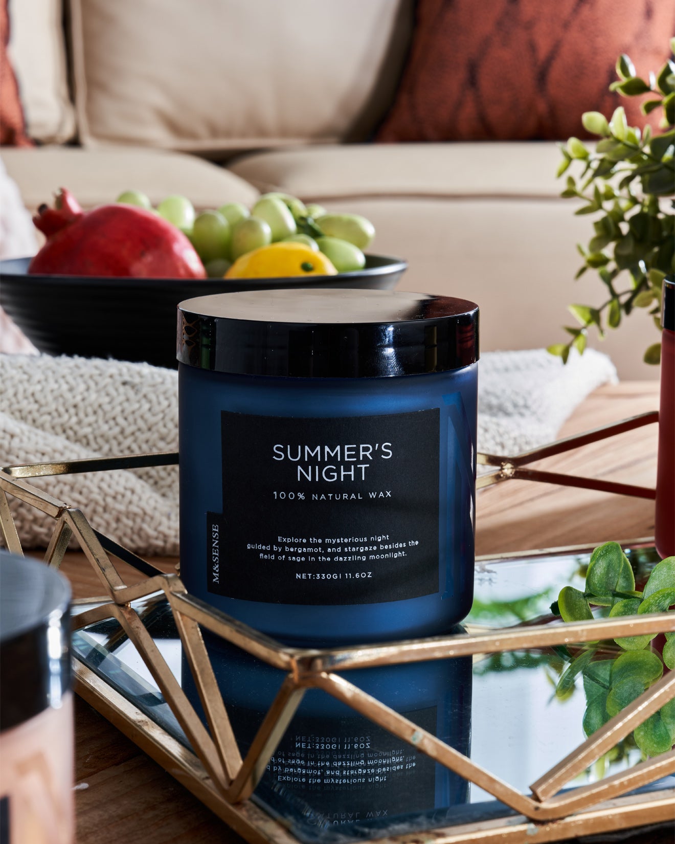 Summer's Night candle on a table with fruit bowl, enhancing a cozy living room with sofa.