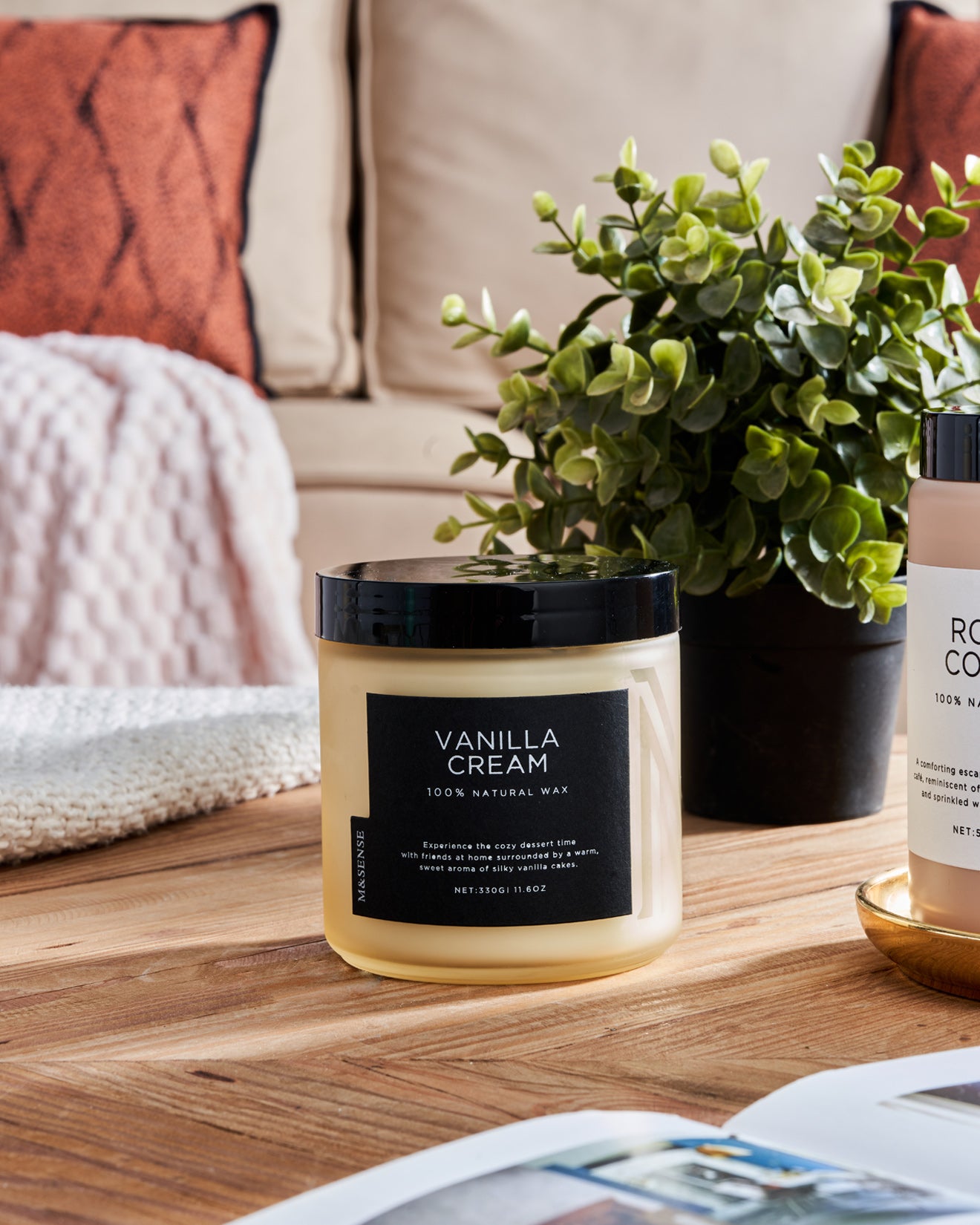 vanilla cream scented candle on wooden table with plant and cozy home decor.