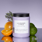 Candle labeled 'Lavender Citrus' with lavender, oranges, and limes on a reflective surface.