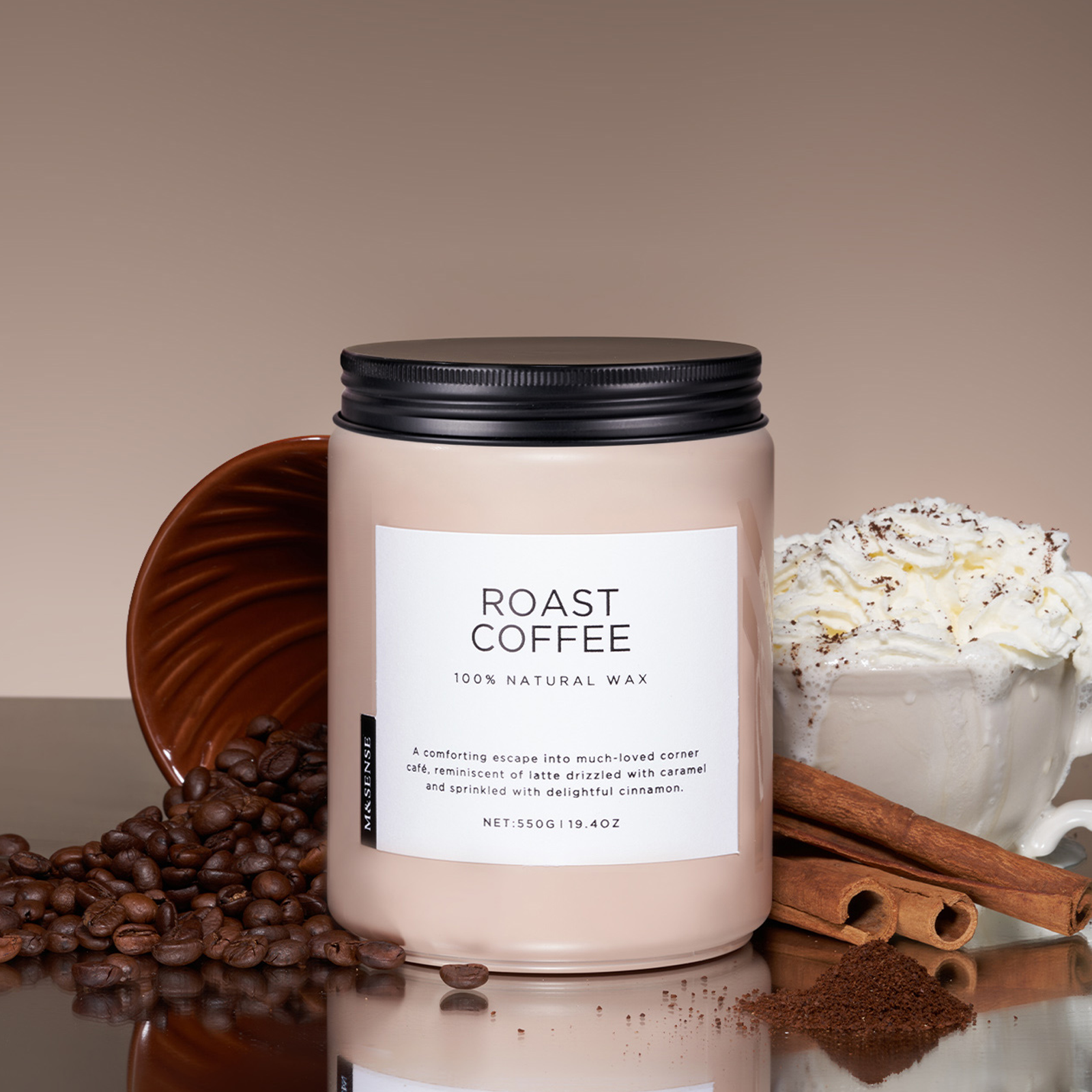 Candle labeled 'Roast Coffee' with coffee beans, a mug of hot chocolate, and cinnamon sticks on a reflective surface.