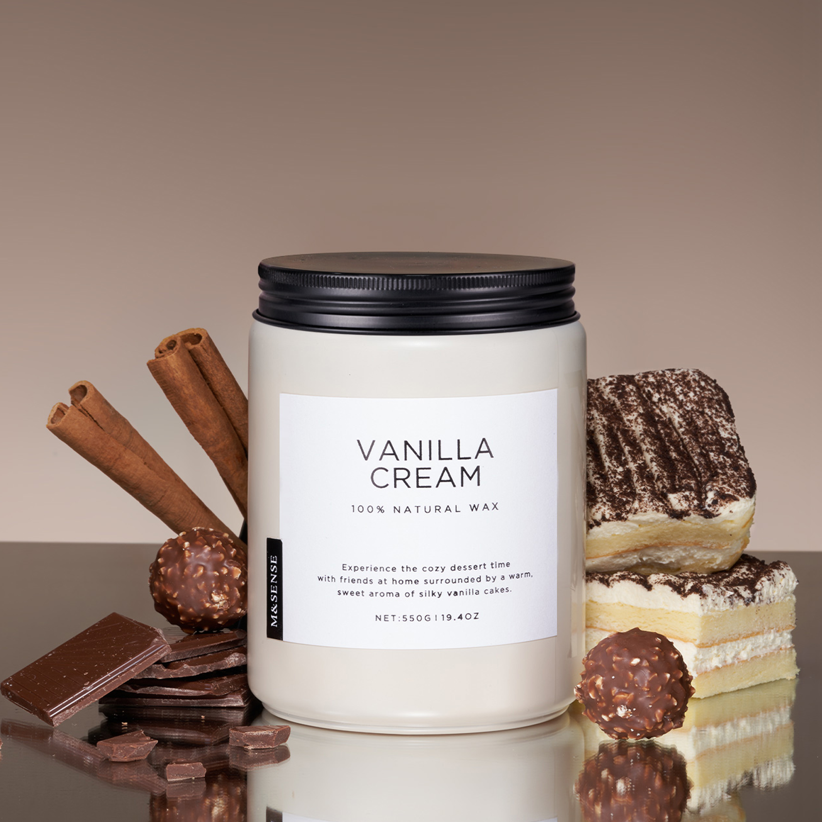 Vanilla cream candle with cinnamon sticks, chocolate, and a slice of cake on a reflective surface.
