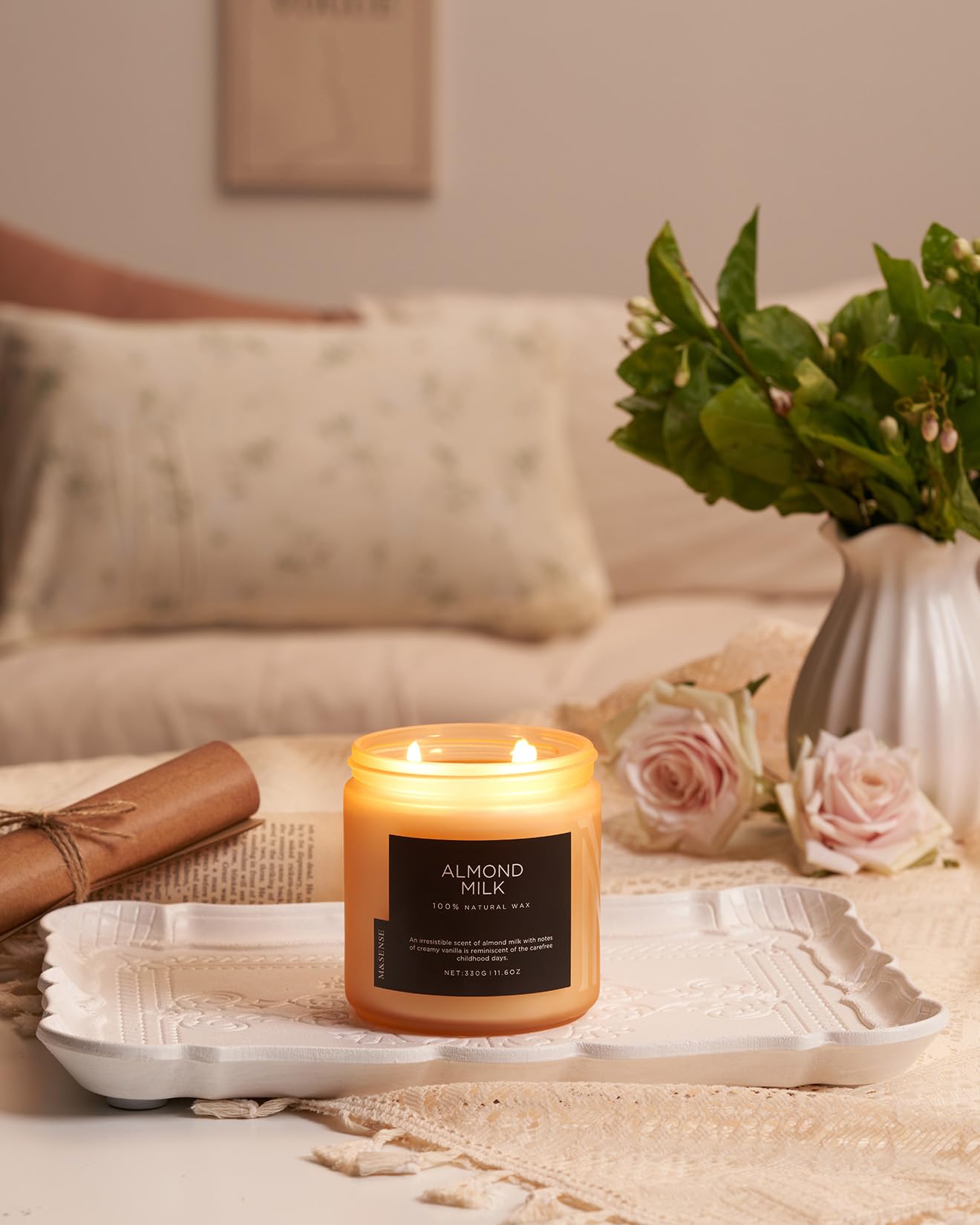 Candle labeled 'Almond Milk' on a tray with flowers and a couch in the background