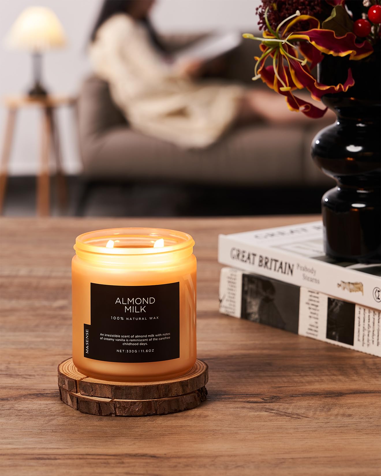 Candle labeled 'Almond Milk' on a wooden coaster with a blurred background of a cozy living room.