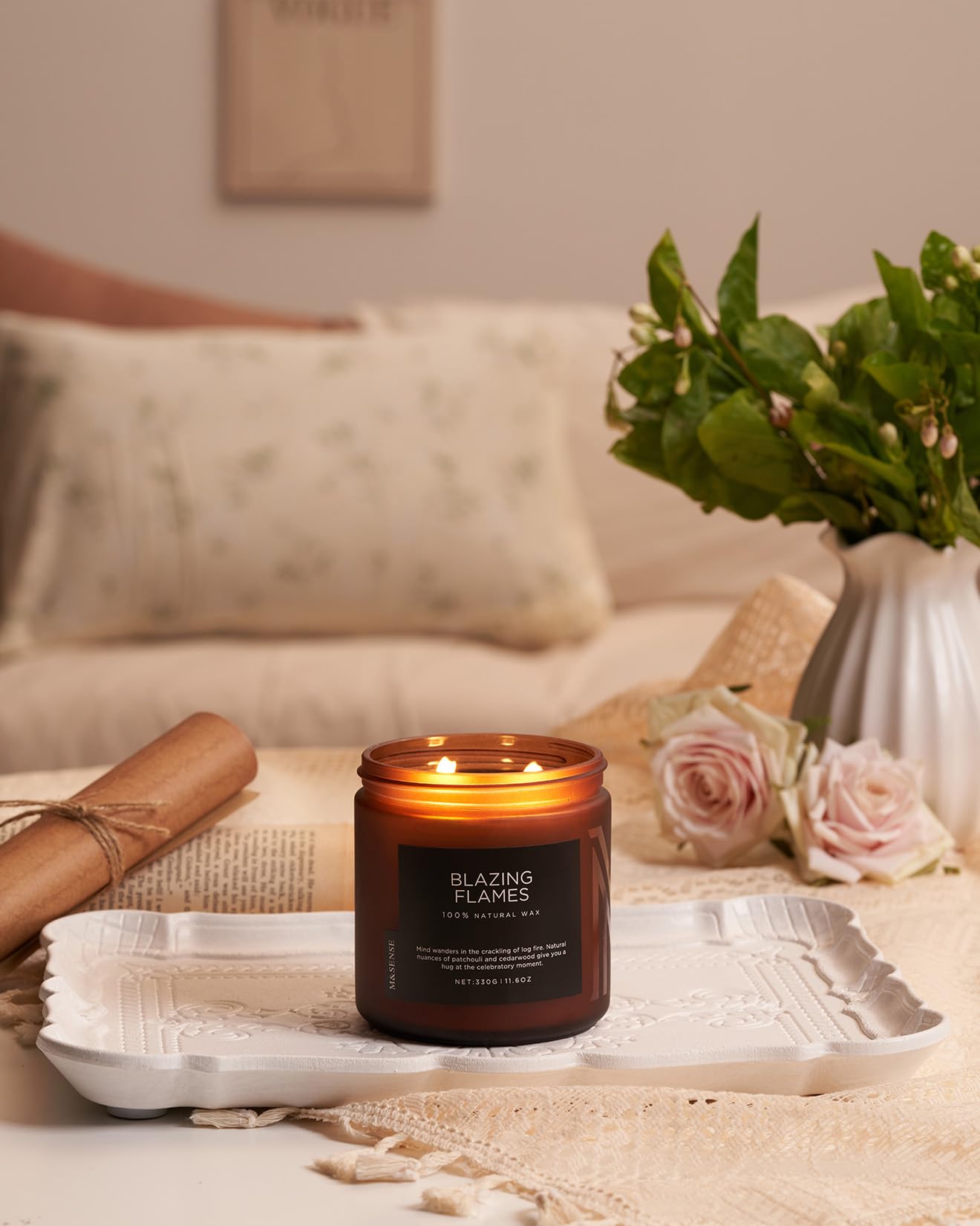 Candle labeled 'Blazing Flames' on a table with flowers and a vase in the background