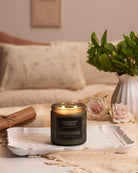 Candle labeled 'Cardamom Cypress' on a tray with flowers and a vase in the background