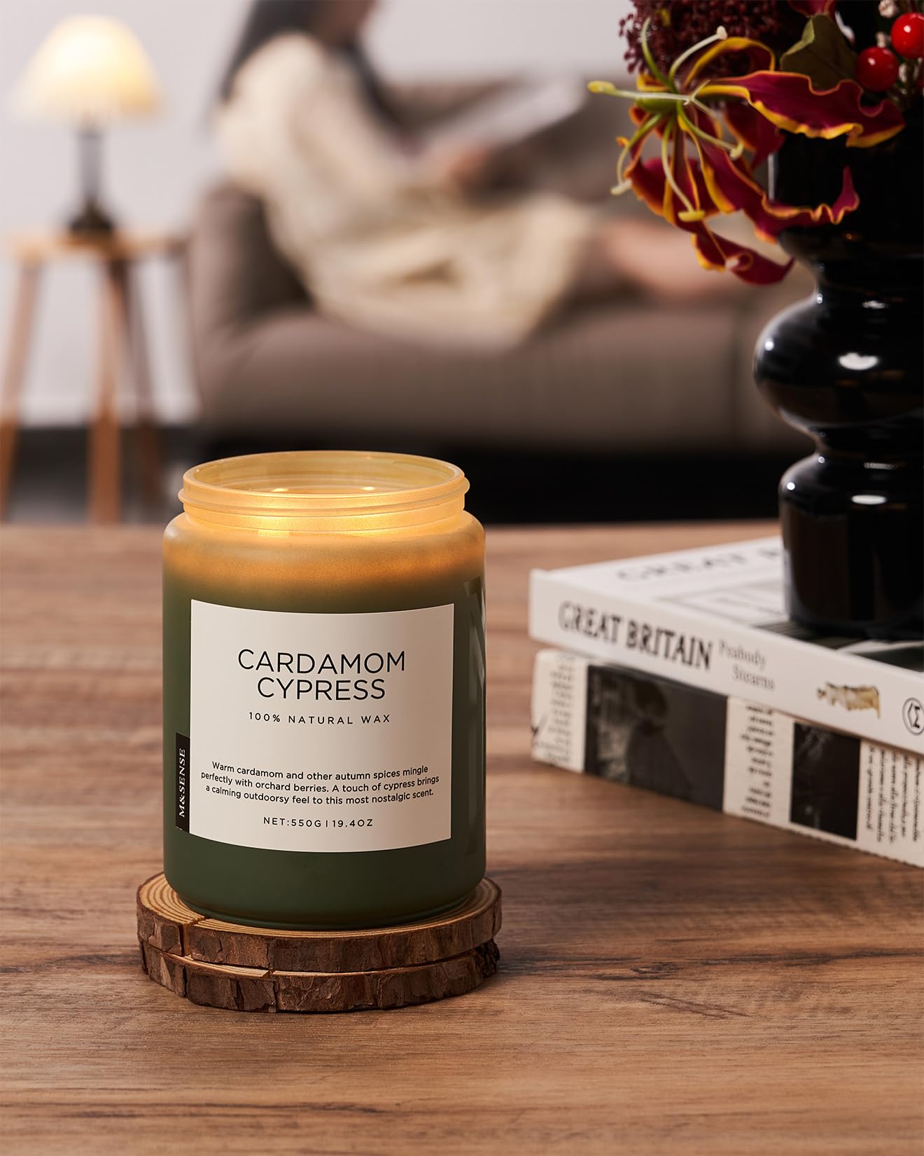Cardamom Cypress candle on a wooden coaster with a blurred background of a living room.