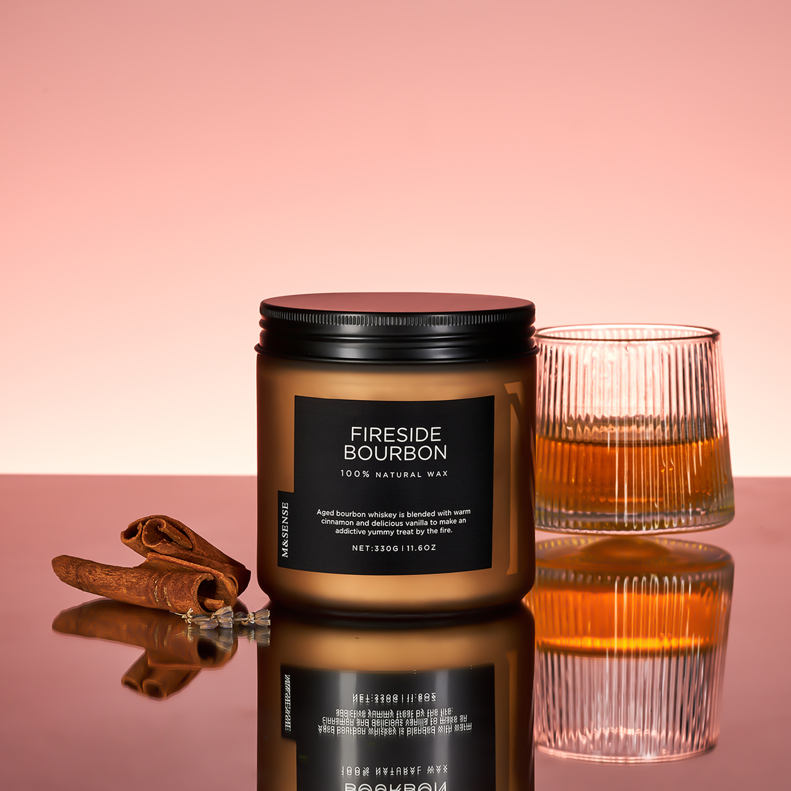 Candle labeled 'Fireside Bourbon' with a glass of whiskey and cinnamon sticks on a reflective surface.