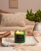 Green candle labeled 'Fraser Fir & Orange' on a tray with flowers and a vase in the background.