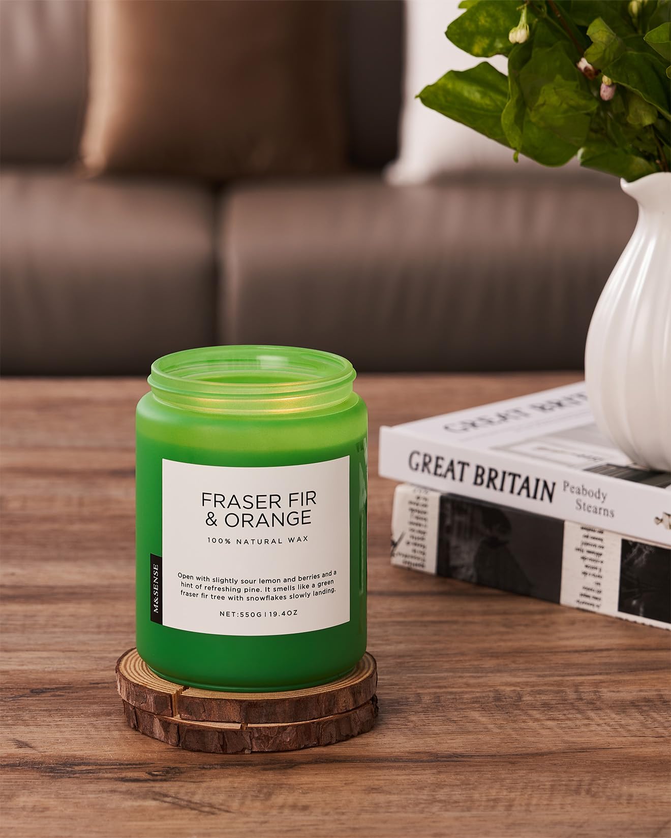 Green candle labeled 'Fraser Fir & Orange' on a wooden coaster with a blurred background