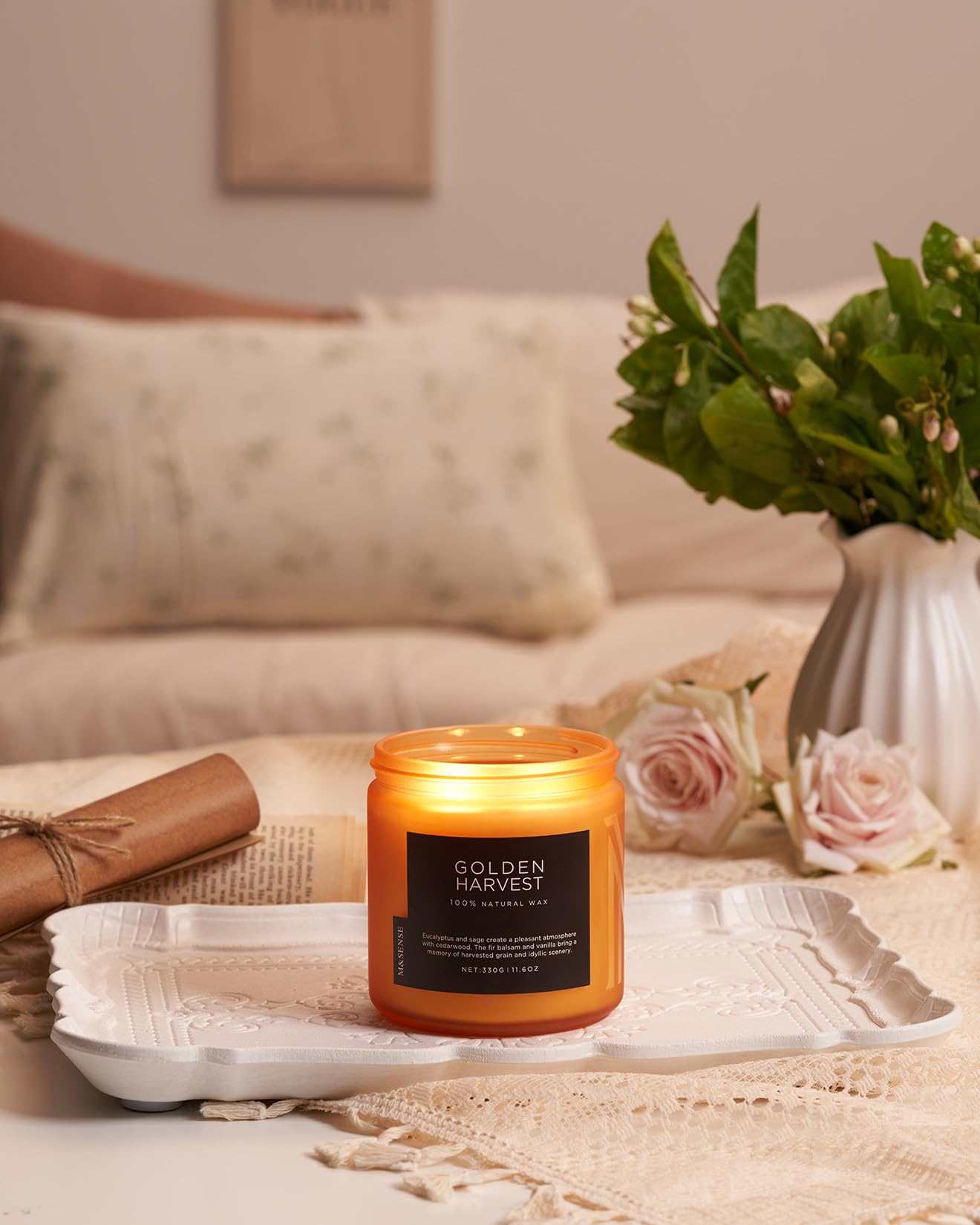 Candle labeled 'Golden Harvest' on a table with flowers and a blanket in the background