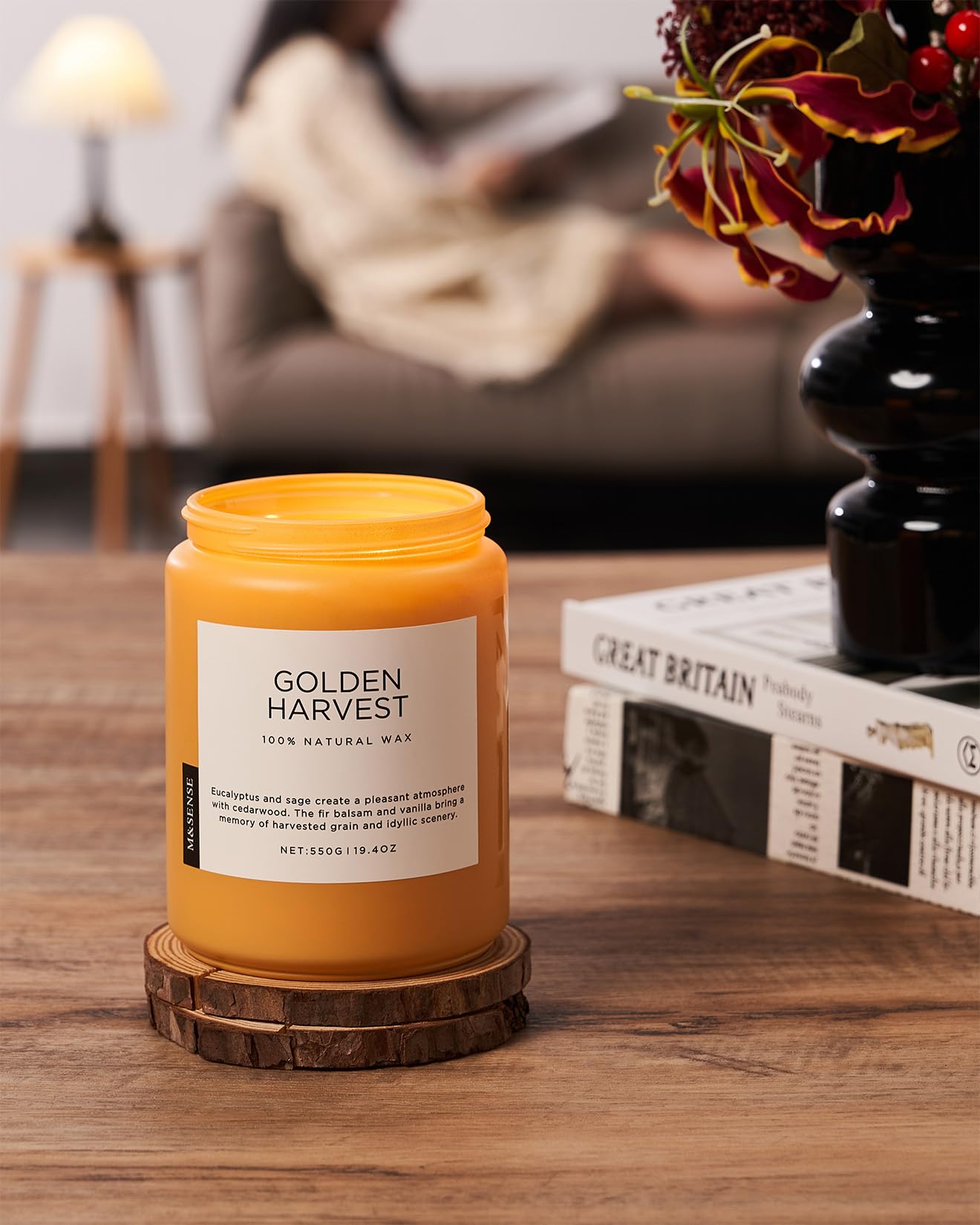 Yellow candle labeled 'Golden Harvest' on a wooden coaster with a blurred background of a cozy living room.