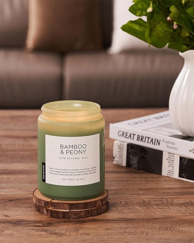 Green candle labeled 'Bamboo & Peony' on a wooden coaster with a couch and plant in the background.