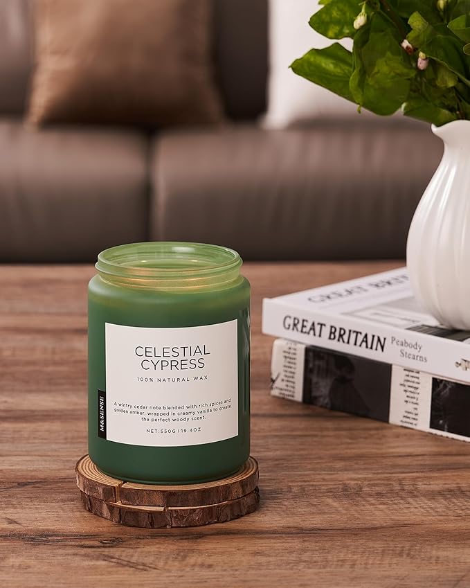 Green candle labeled 'Celestial Cypress' on a wooden coaster with a couch and vase in the background.