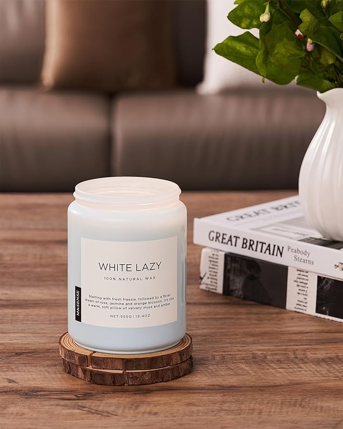 Candle labeled 'White Lazy' on a wooden coaster with a blurred sofa and plant in the background