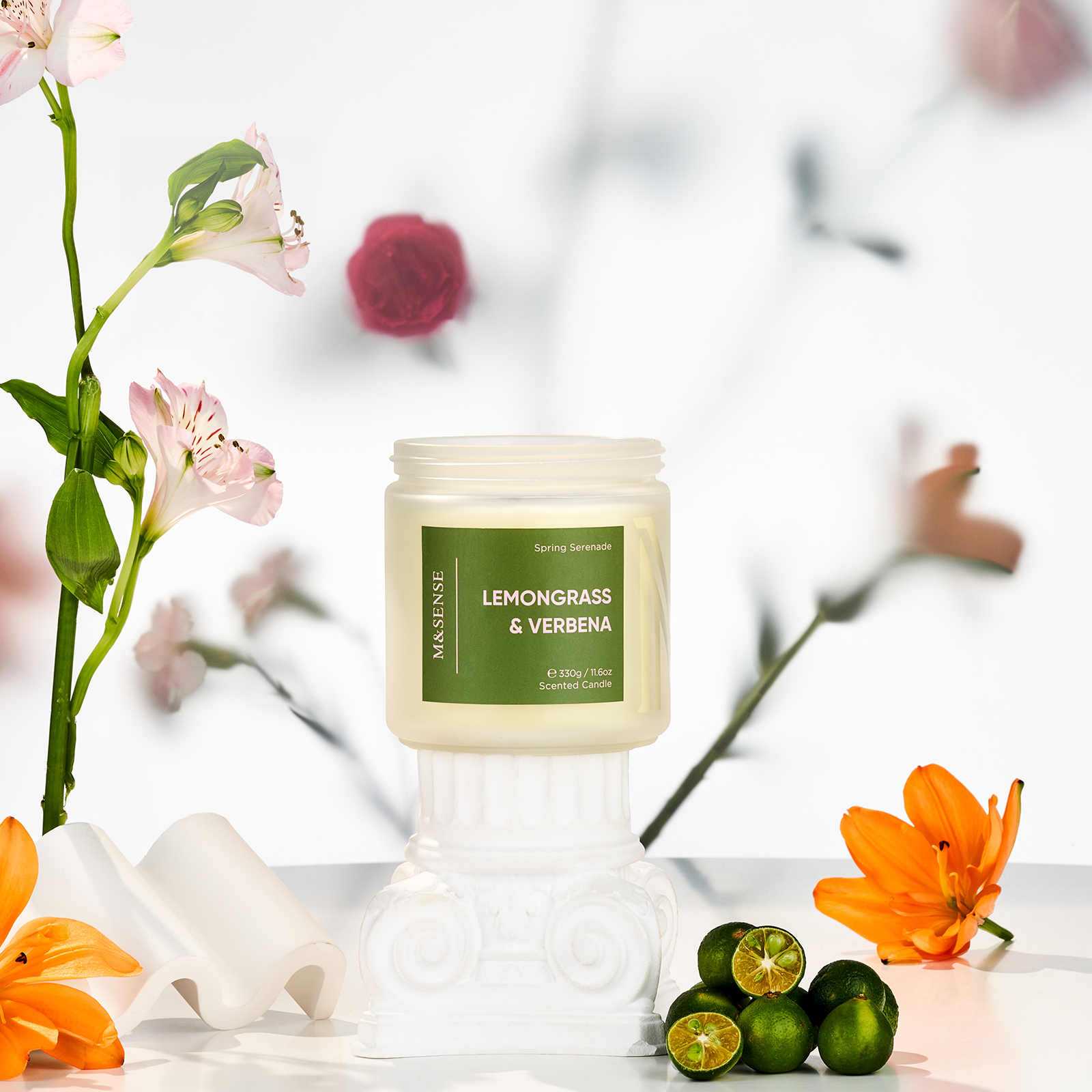 Candle labeled 'Lemongrass & Verbena' with flowers and limes on a blurred background
