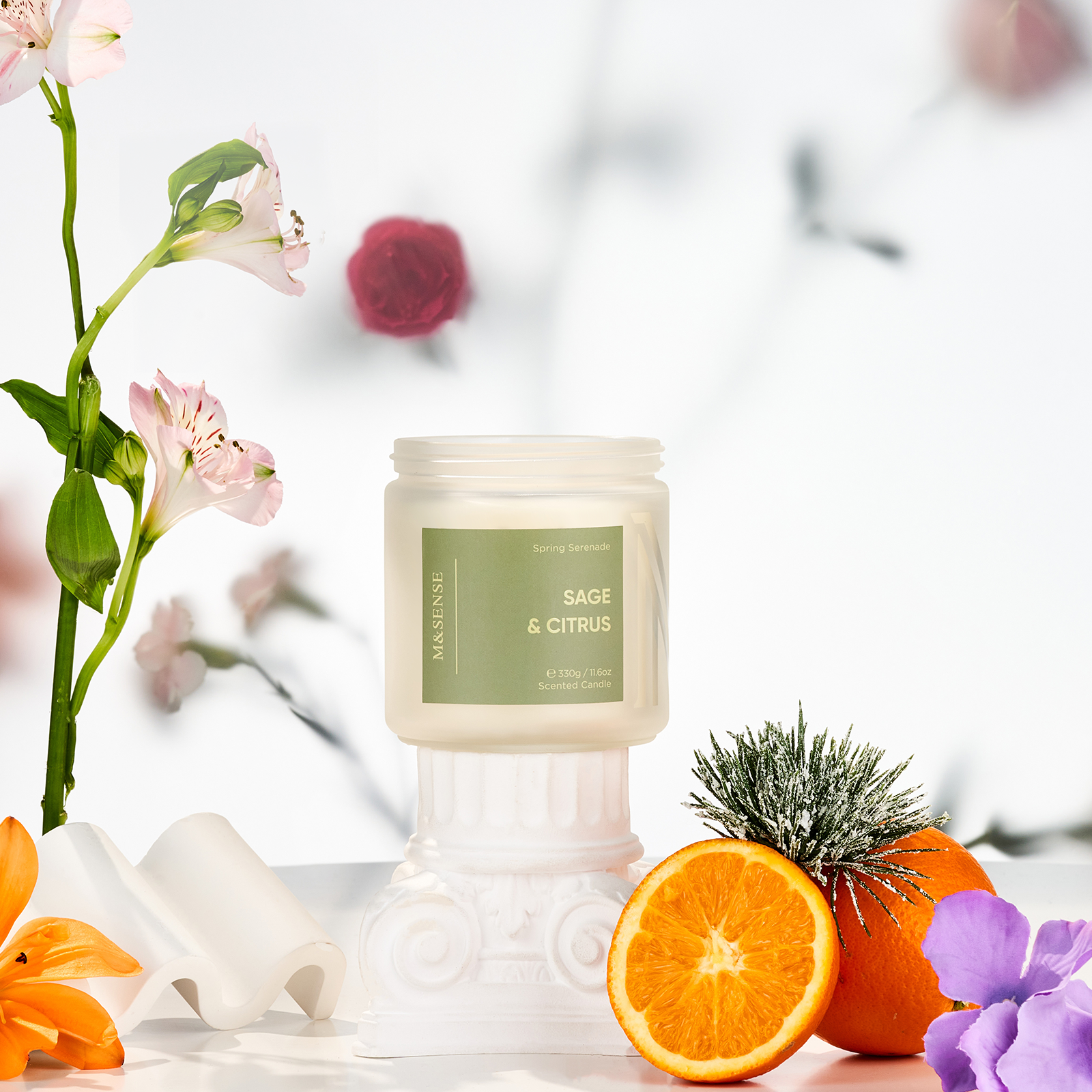 Candle labeled 'Sage & Citrus' with flowers and oranges on a light background