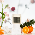 Candle labeled 'Sage & Eucalyptus' with flowers and oranges on a light background