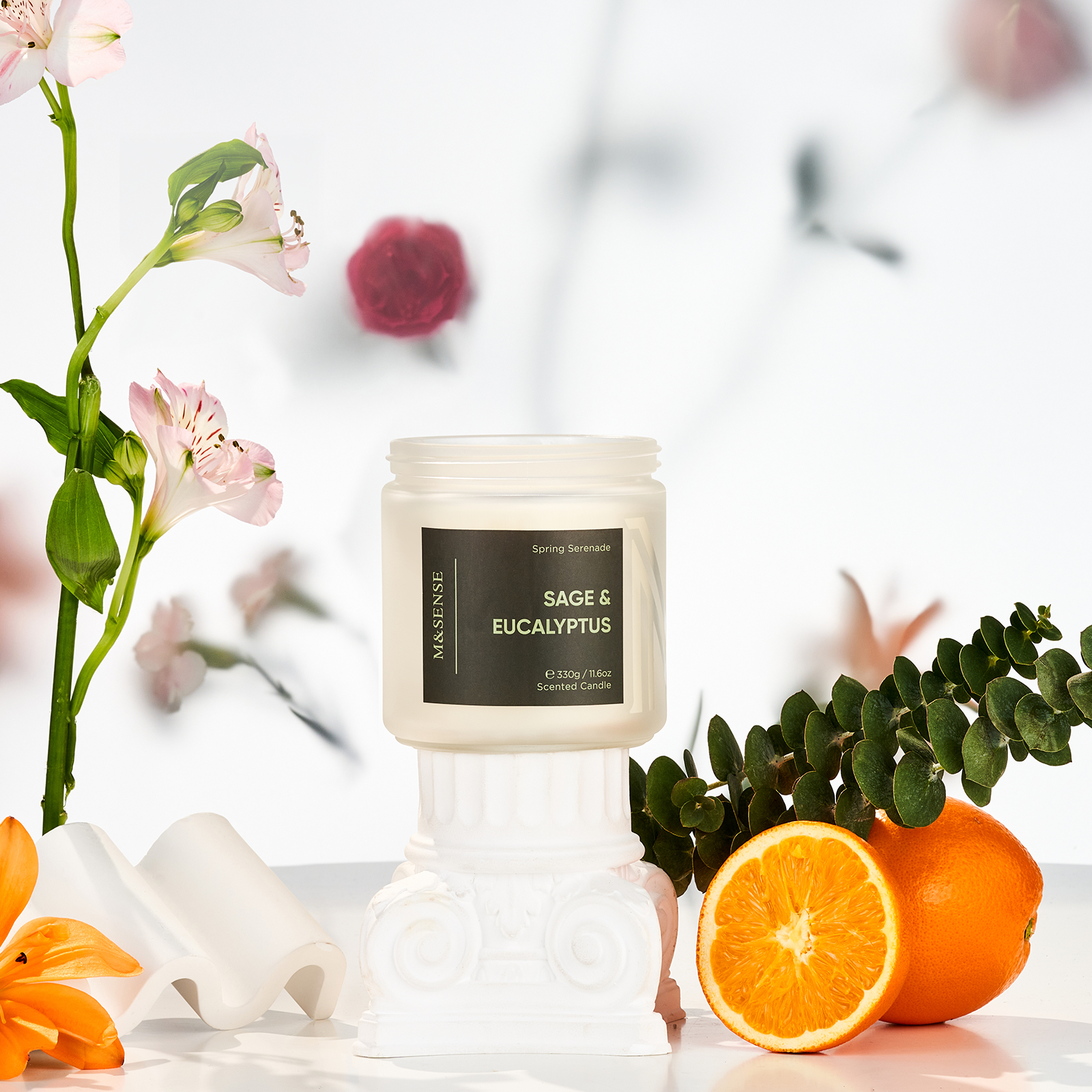 Candle labeled 'Sage & Eucalyptus' with flowers and oranges on a light background