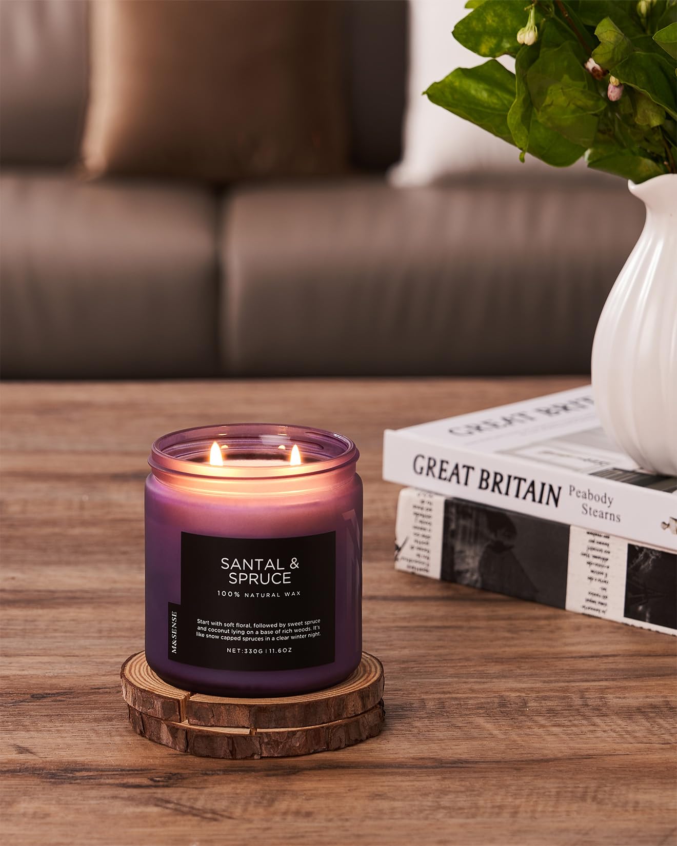 Scented candle with wooden coaster on a table with a blurred sofa and book in the background