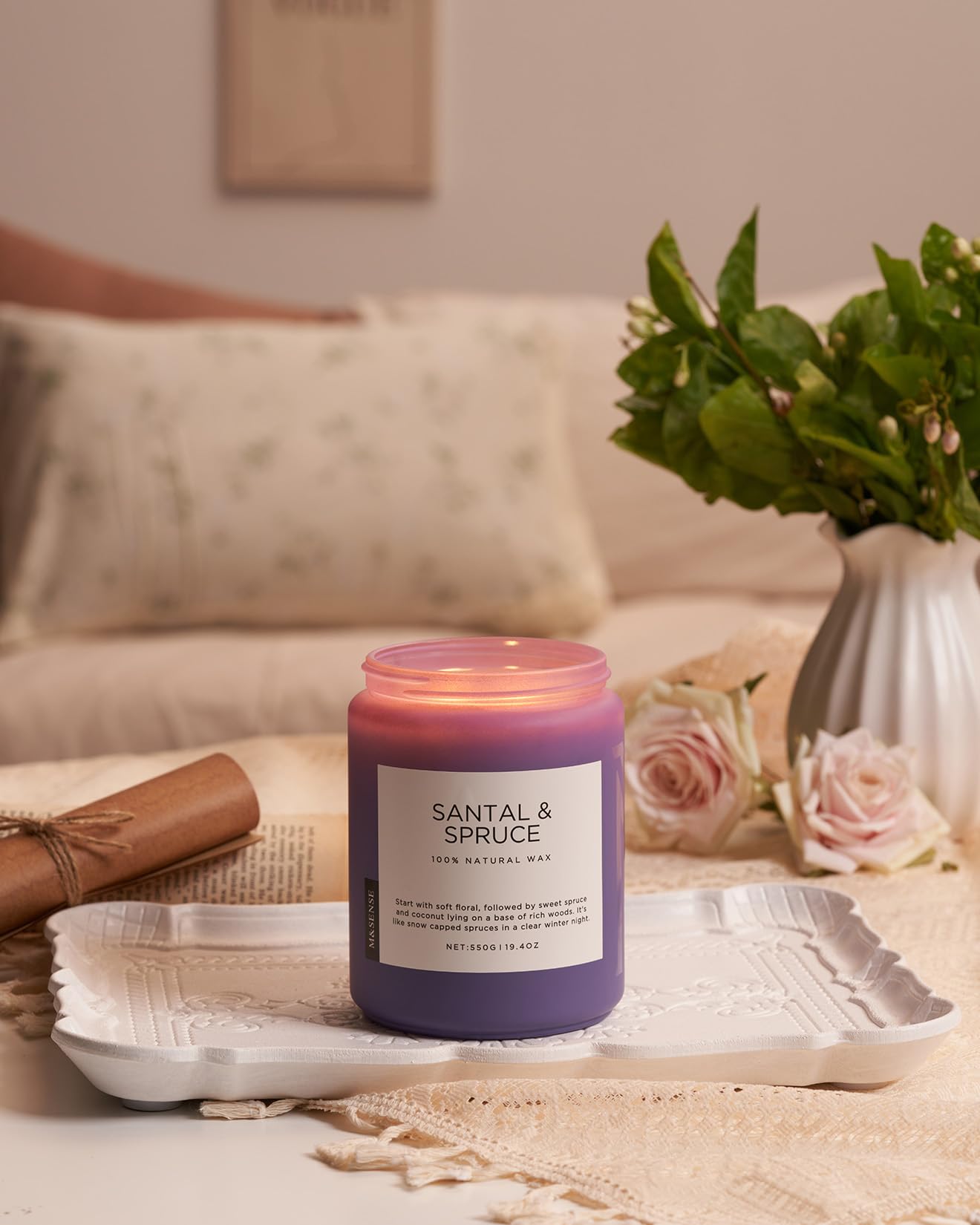 Santal & Spruce candle on a table with flowers and a blanket in the background