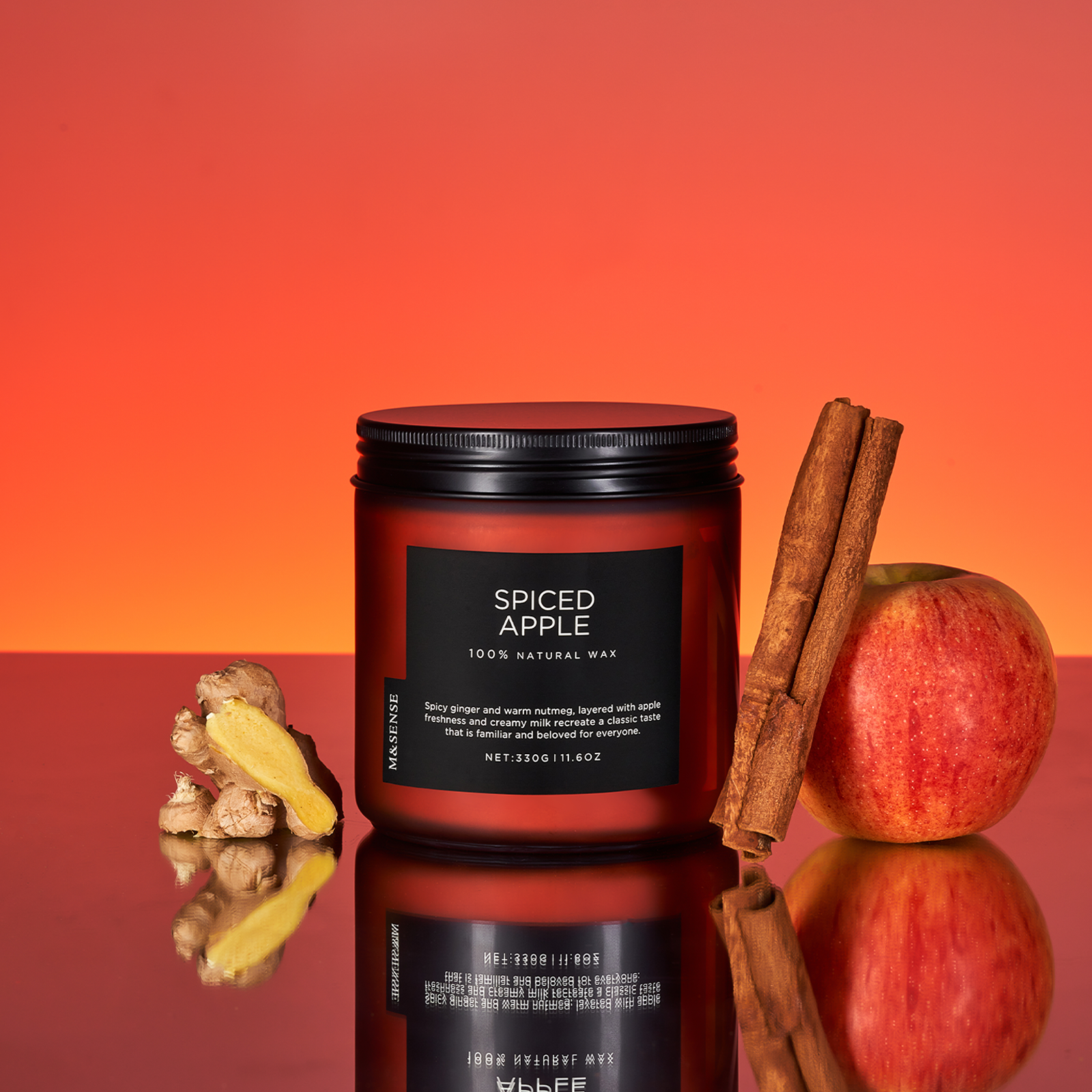 Spiced Apple candle with ginger, apple, and cinnamon sticks on a reflective surface with an orange gradient background.
