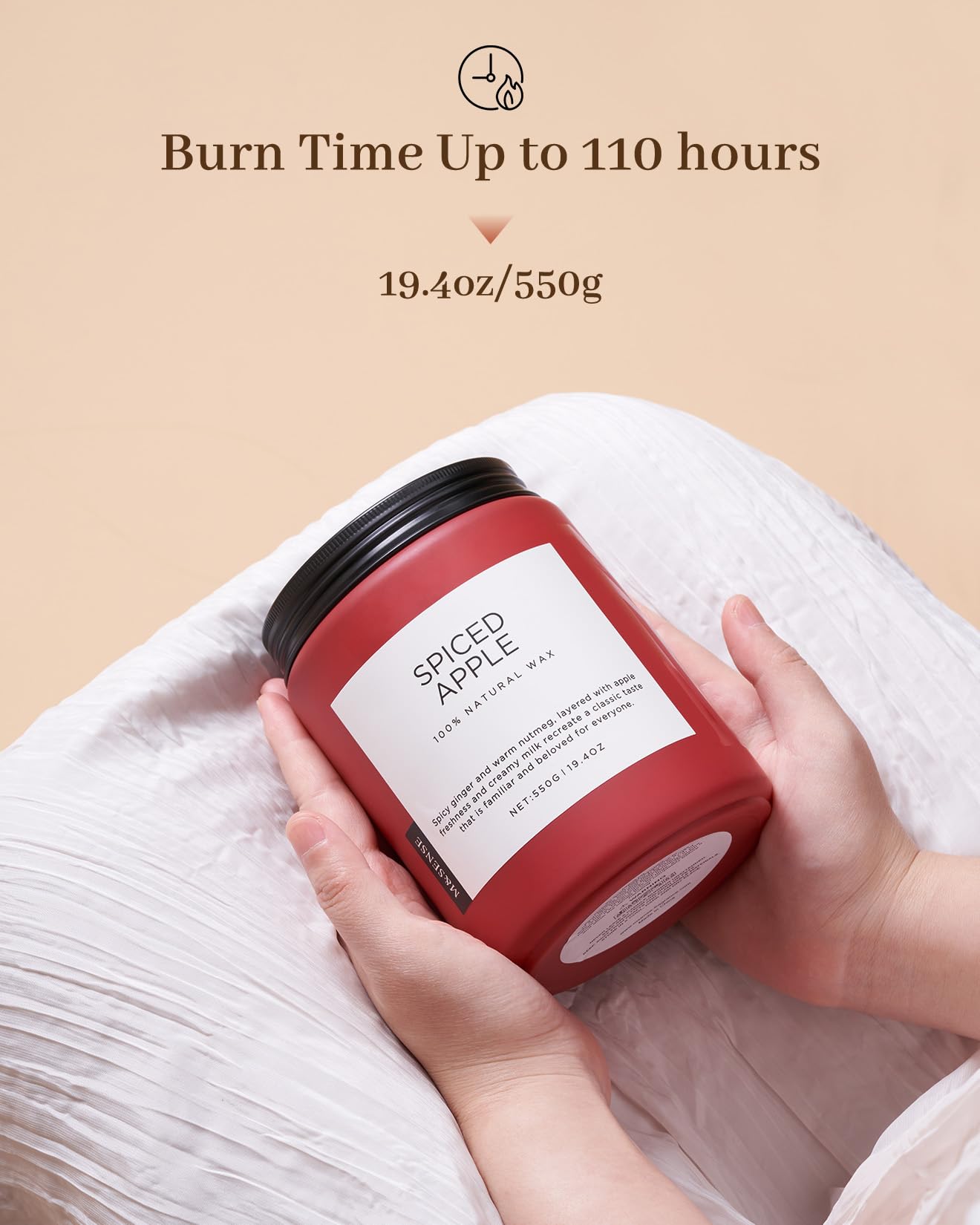 Red candle labeled 'Spiced Apple' held by hands on a beige background