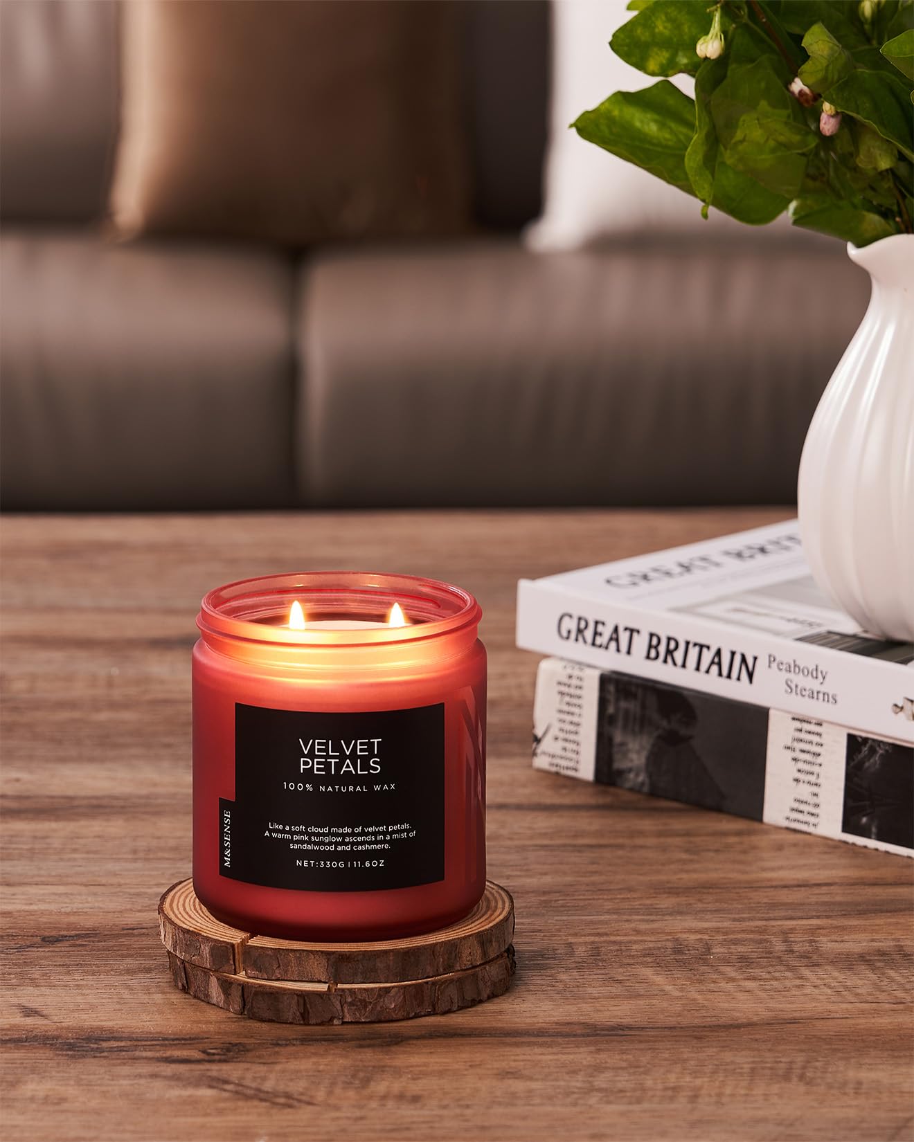 Red candle with a wooden coaster on a table, with a blurred background of a couch and books.