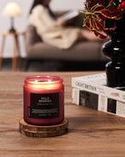 Candle labeled 'Wild Berries' on a wooden coaster with a blurred background of a person reading a book.